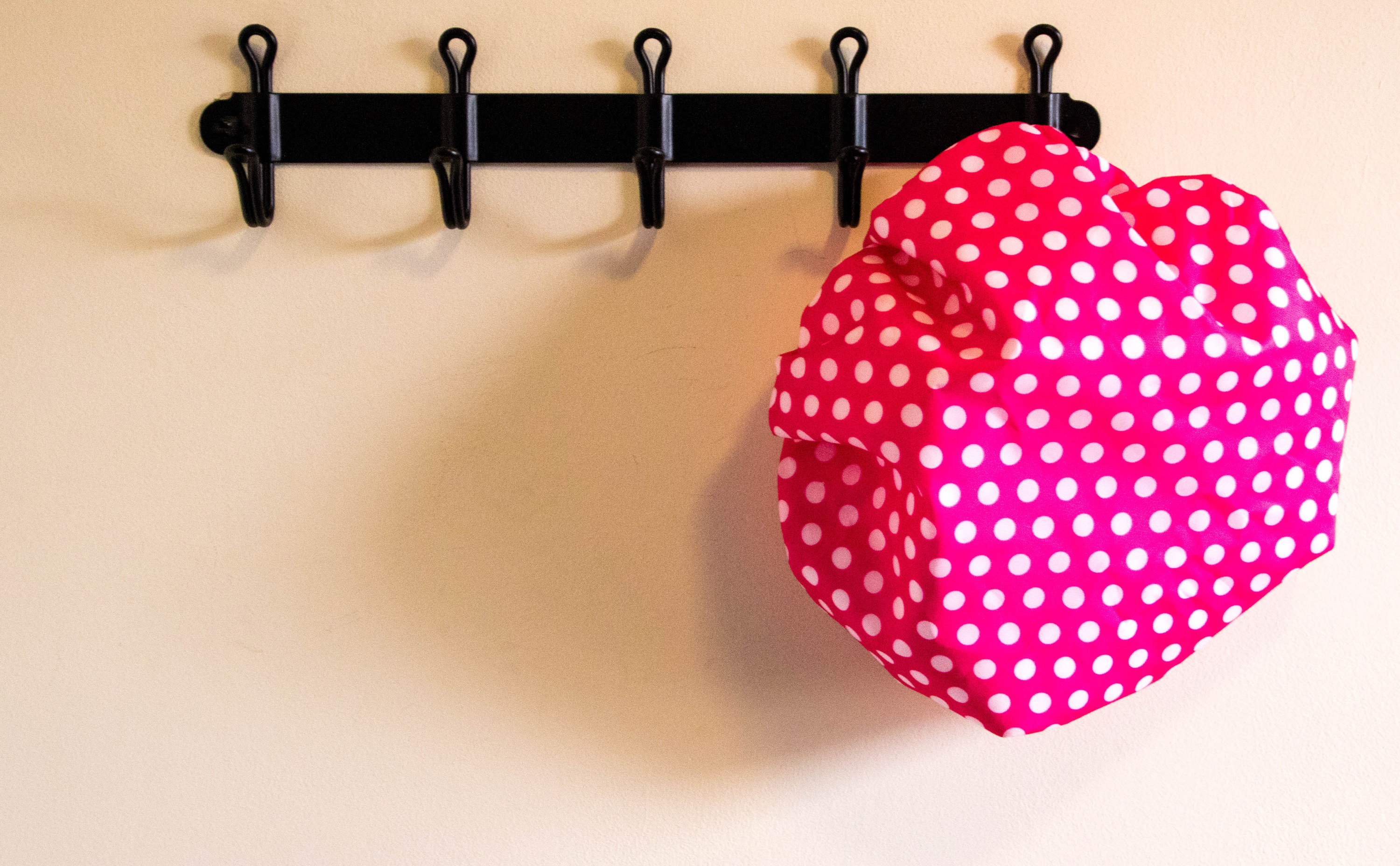 A pink and white polka dot shower cap hanging on a black hook