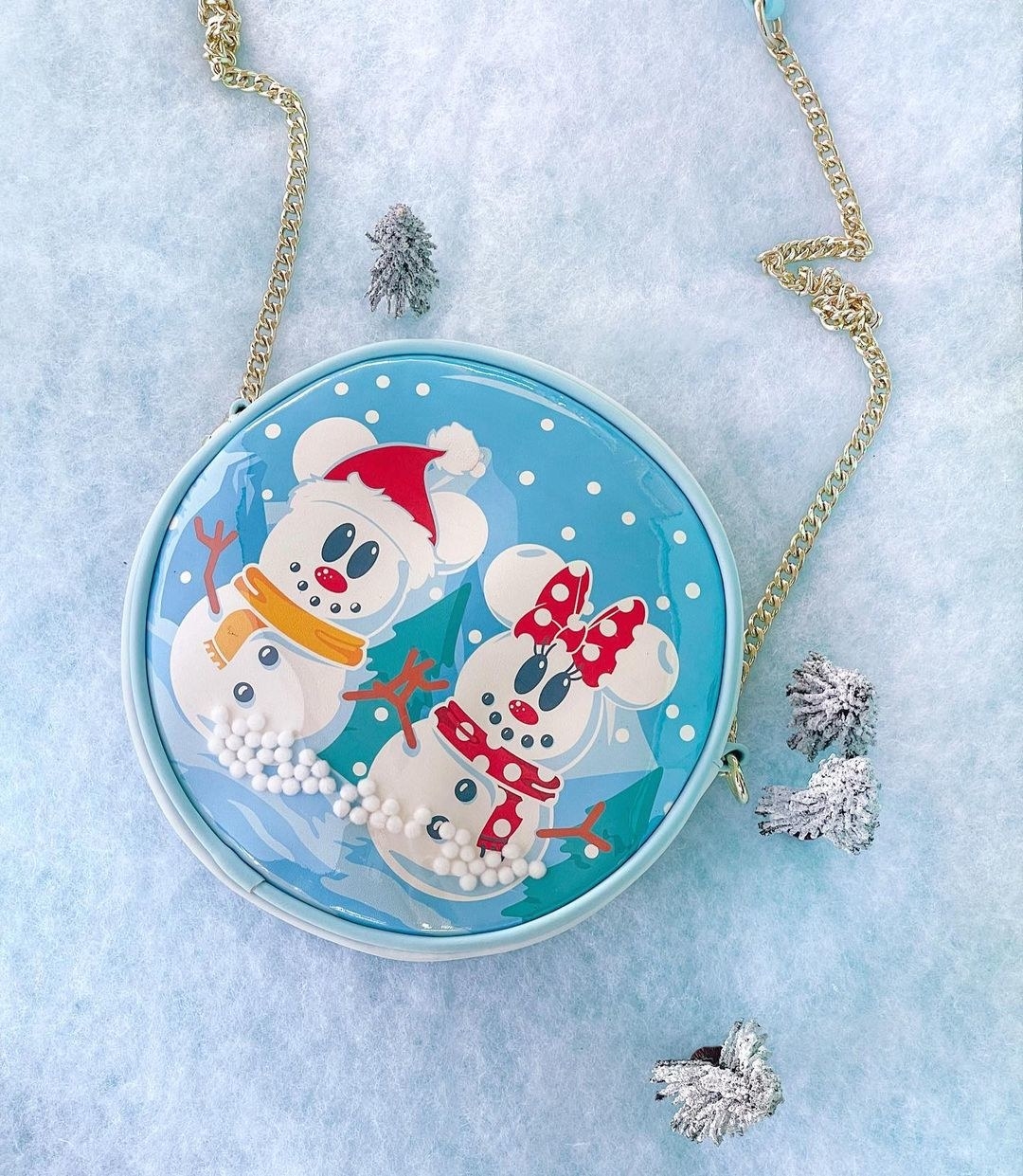 a round blue crossbody bag with falling snow inside and mickey and minnie as snowmen