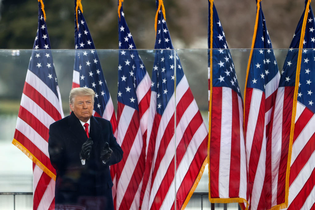 Trump standing onstage in front of a row of American flags at the rally