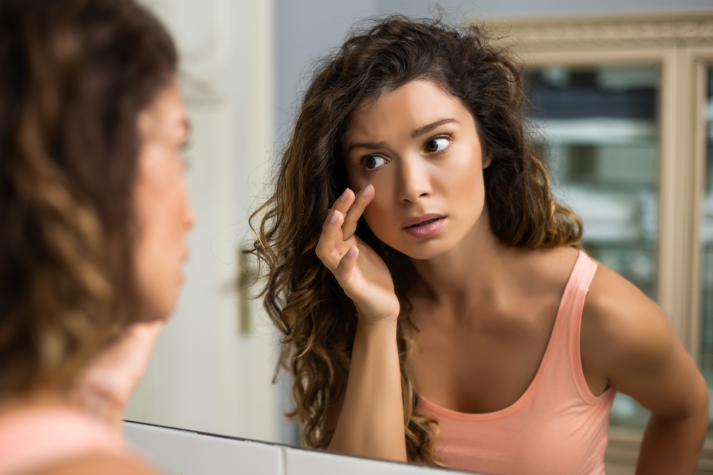 A woman looking in the mirror at her tired eyes