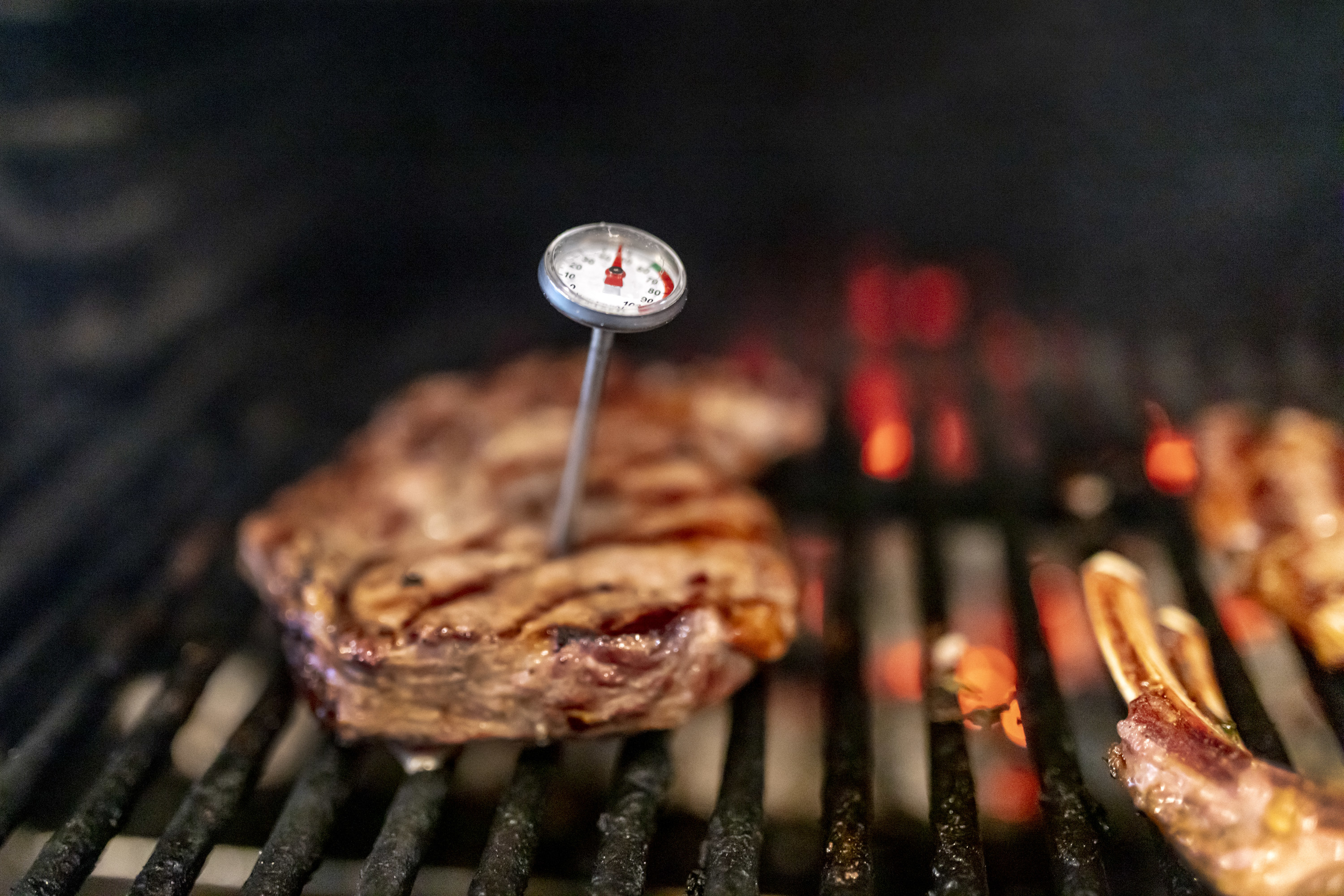 Meat thermometer stuck into a large steak on the grill