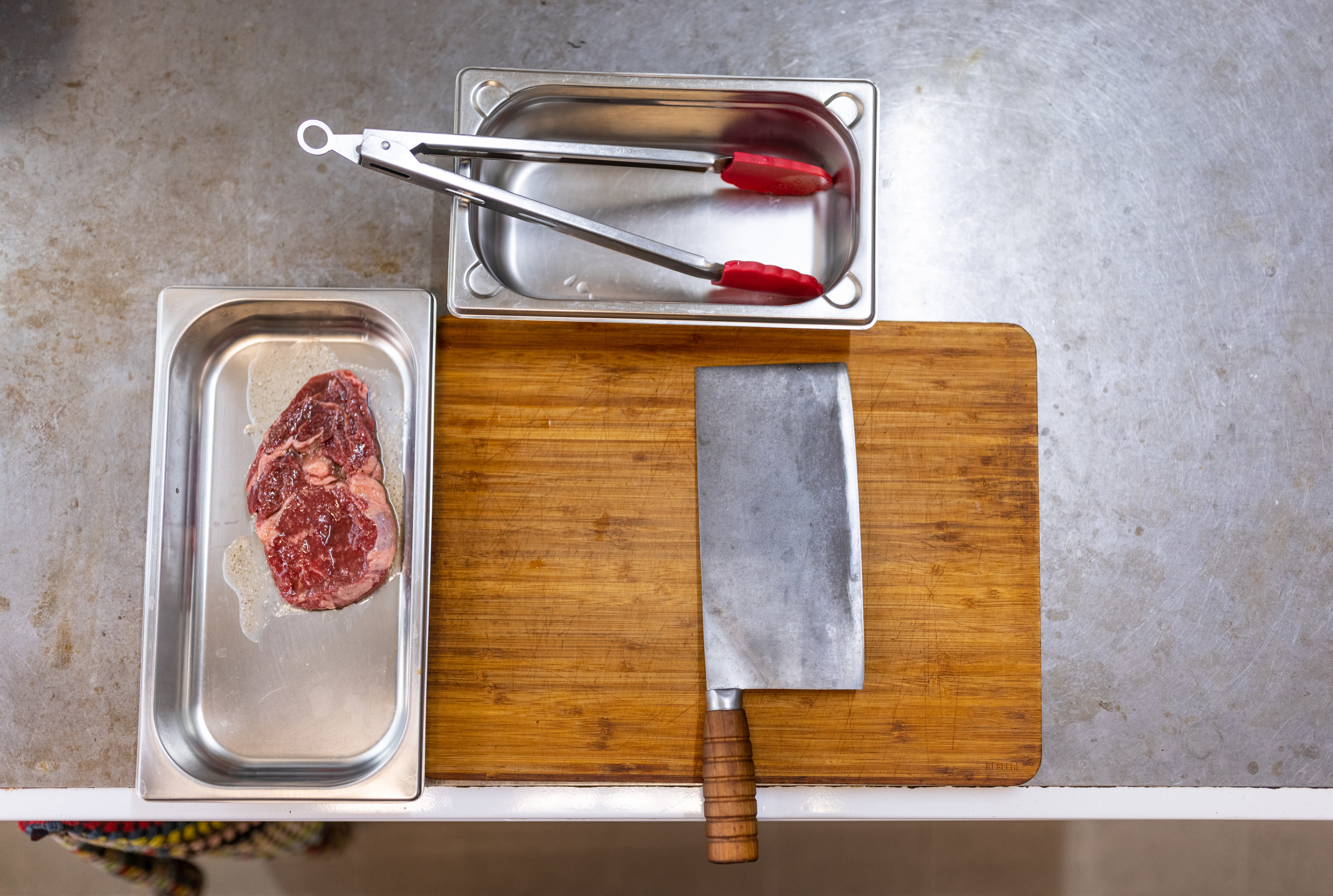 Raw steak laid next to a cutting board with a clever.