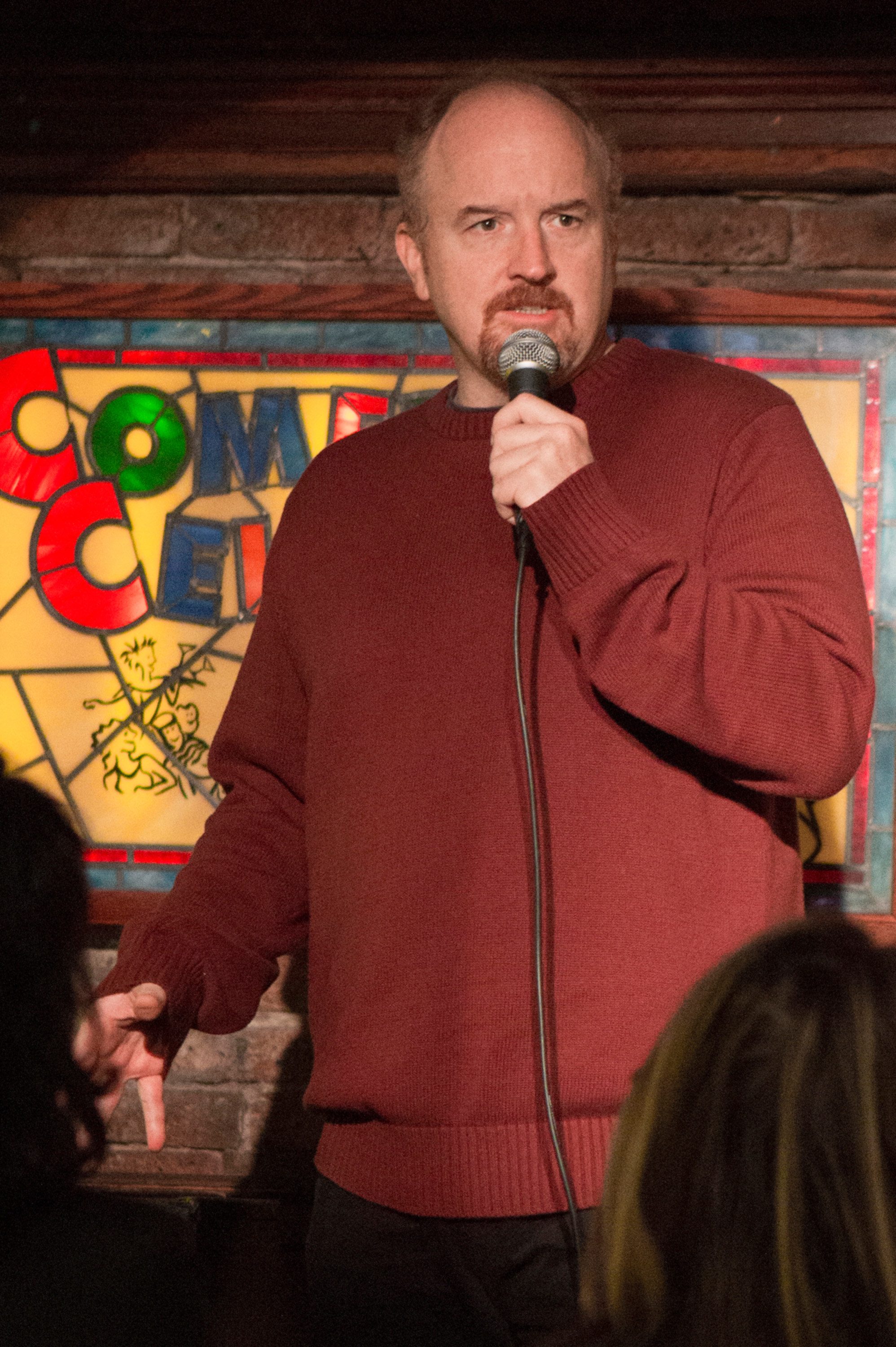 Louie in the show talking into a mic at a bar