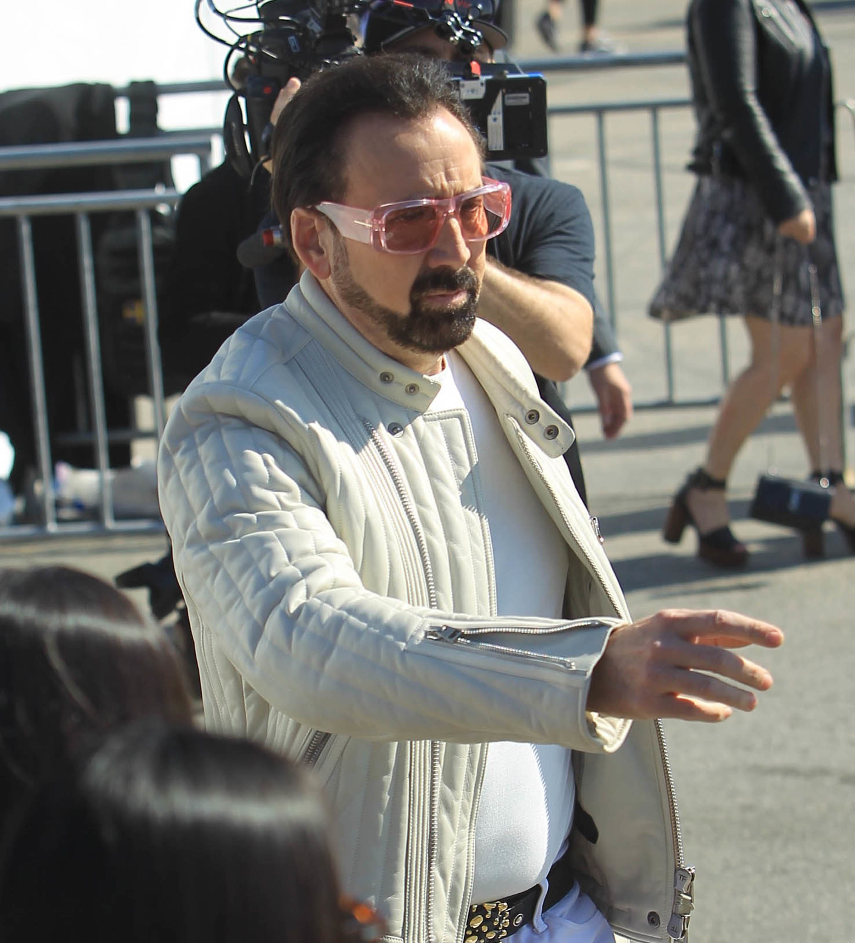 Cage extends his arm while wearing a jacket and sunglasses