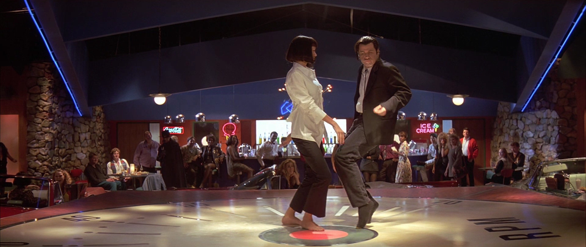 A man and woman dancing on an empty dance floor together in front of a crowd.