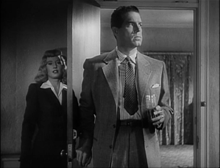 A man walking into a room with a woman hiding behind the door.