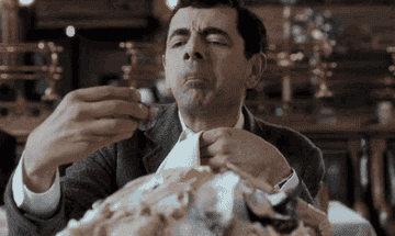 Rowan Atkinson as Mr Bean pretending to enjoy an oyster as he lets it slip into his napkin to avoid eating it