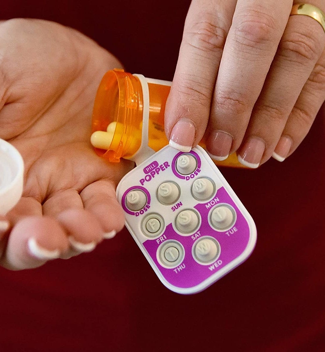 A person holding an open pill bottle with a pill tracker on it