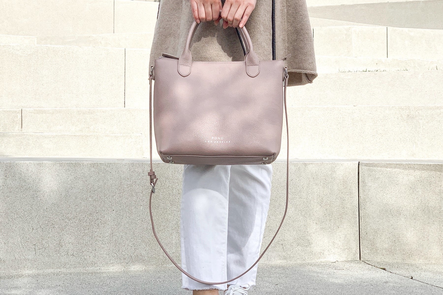 a model holding a blush colored tote bag