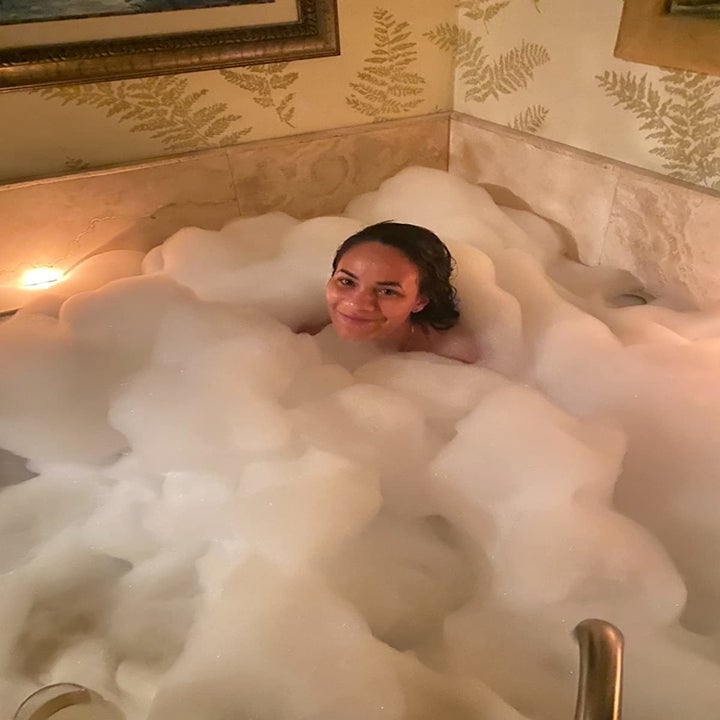 Reviewer sitting in tub of bubbles after using product