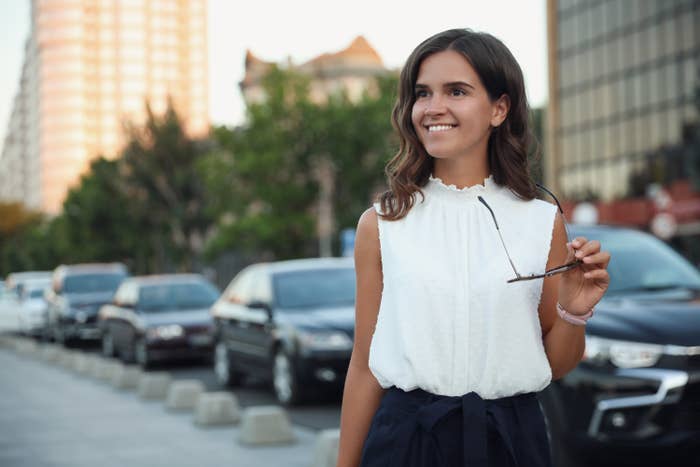 Young woman in a white blouse, smiling and holding sunglasses