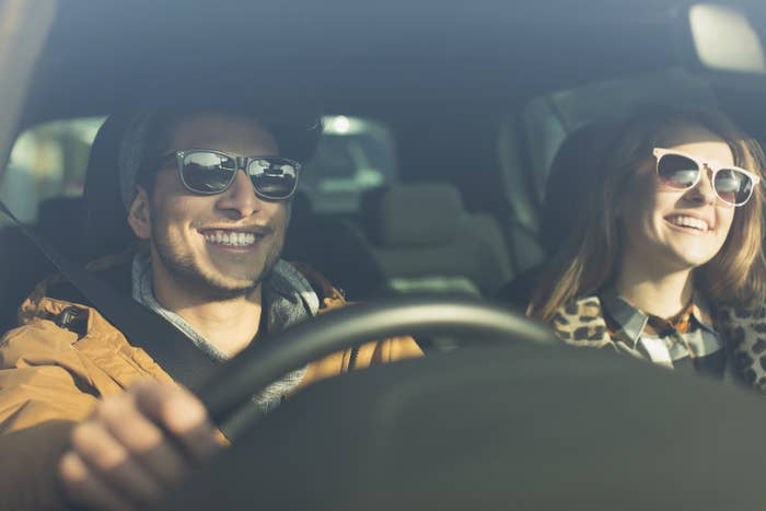 A man and a woman wear sunglasses while driving in the car on a sunny day