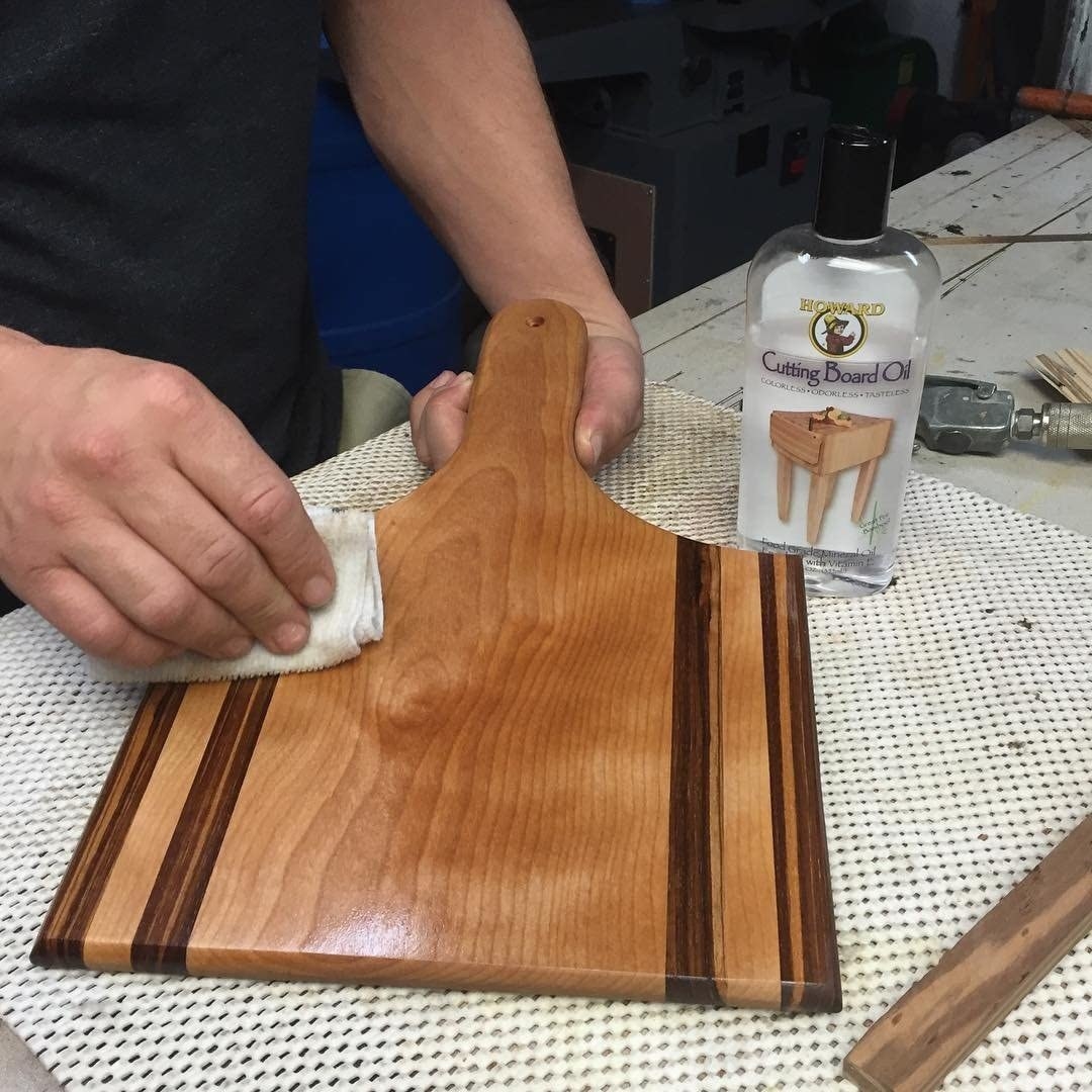 A person wiping down a cutting board with the oil