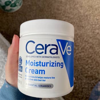 reviewer holding a tub of the moisturizer