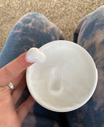 reviewer's finger dipped into the tub of moisturizer