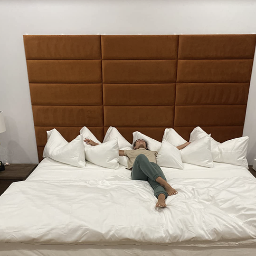 reviewer laying on their bed with the upholstered headboard behind them