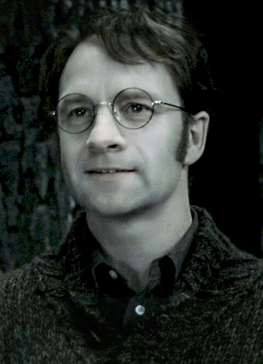 James Potter wears round glasses and a sweater over a button-down shirt, smiling