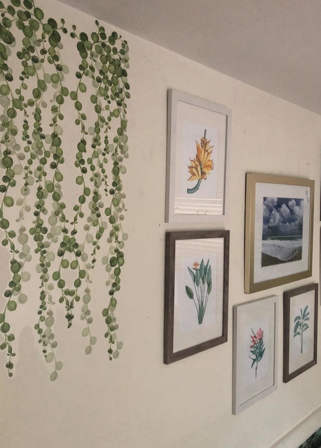 a reviewer photo of the pair of decals on a wall next to several picture frames