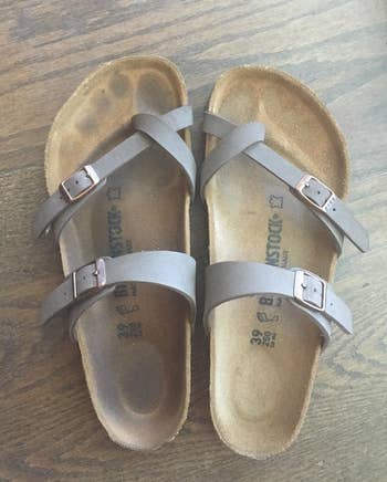 reviewer shows a pair of sandals with suede soles, one has a dirty foot outline and the other is clean after using the brush