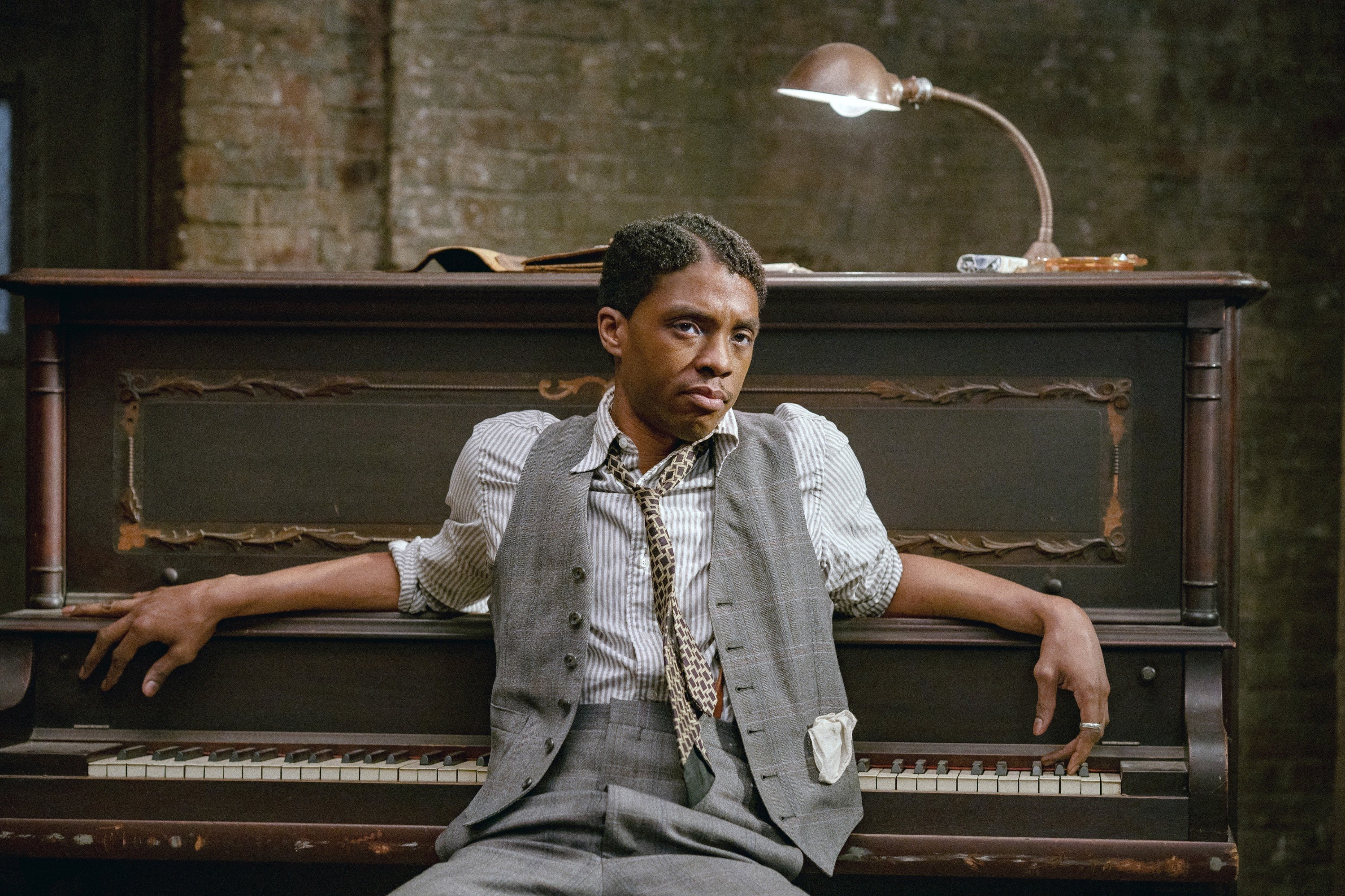 Boseman sits against a piano