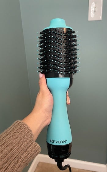 a reviewer holds up the blue hair dryer brush