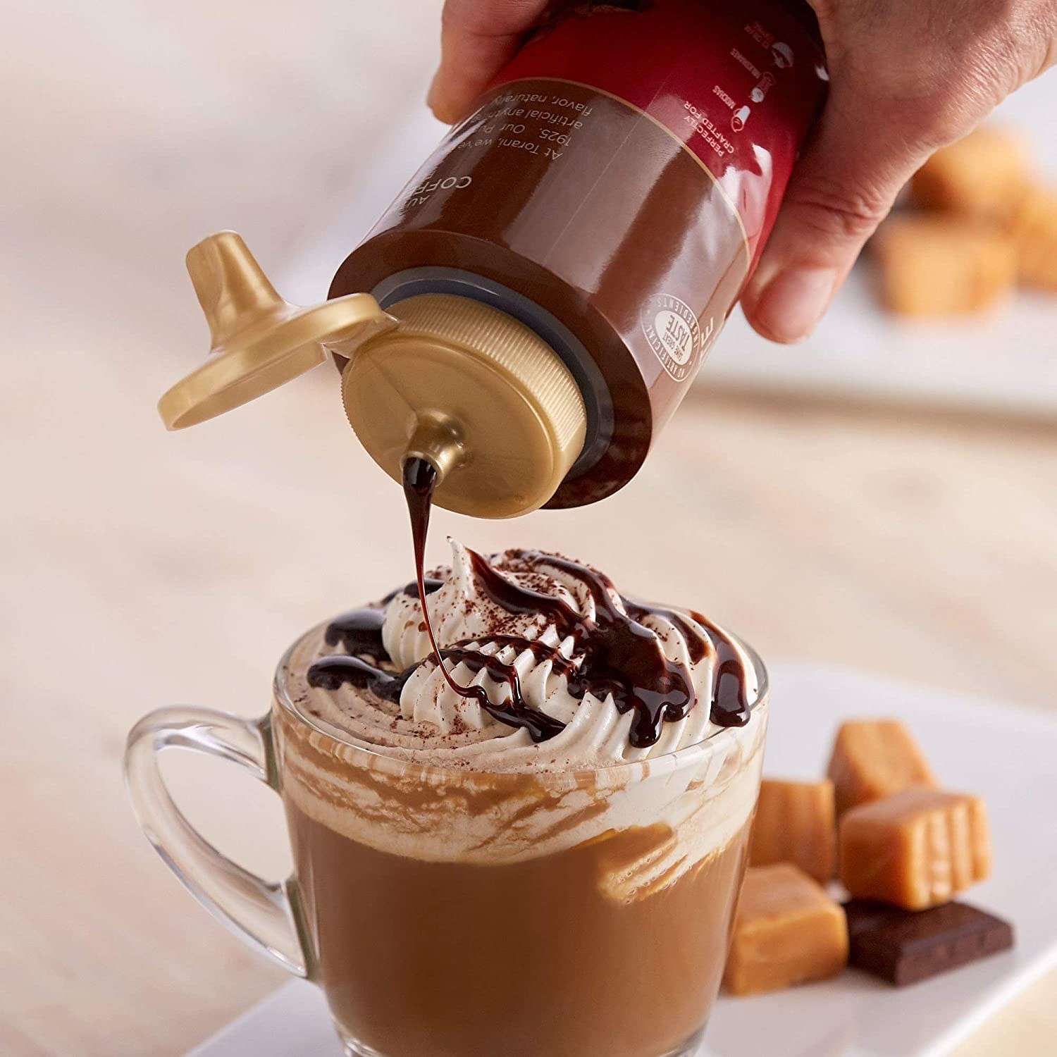A person pouring caramel sauce on their cup of coffee with whipped cream