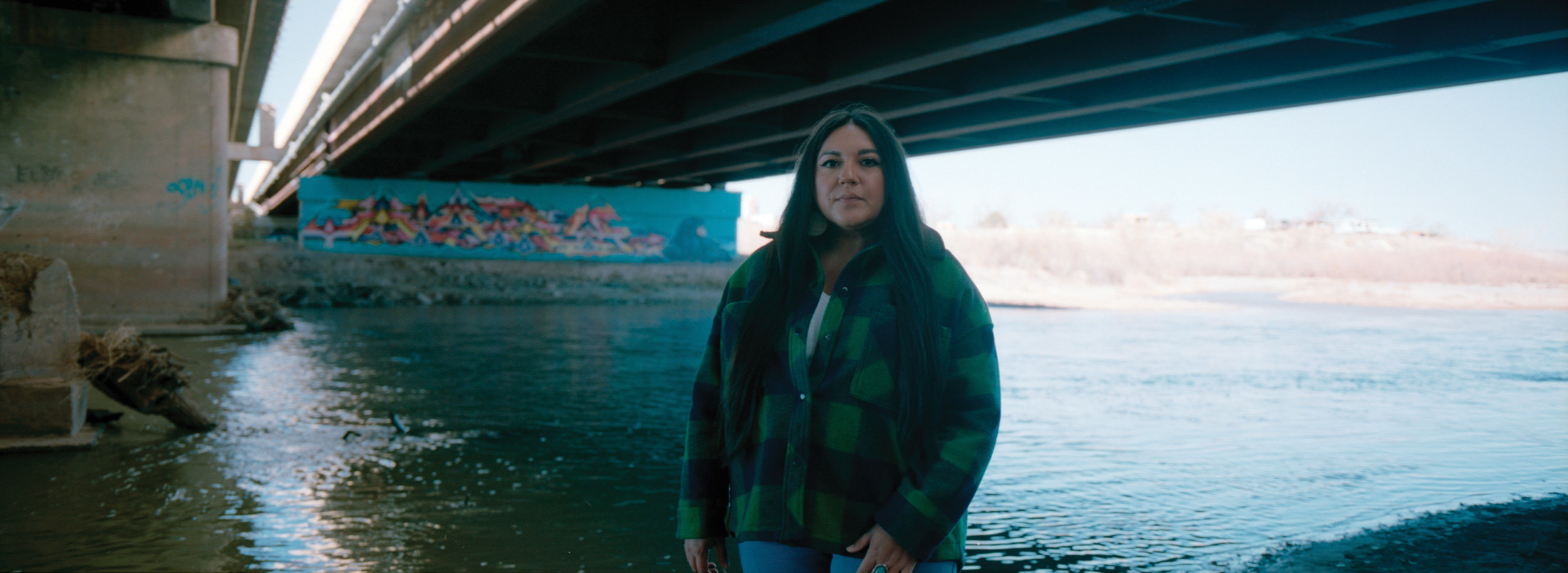 A woman under a bridge by a river