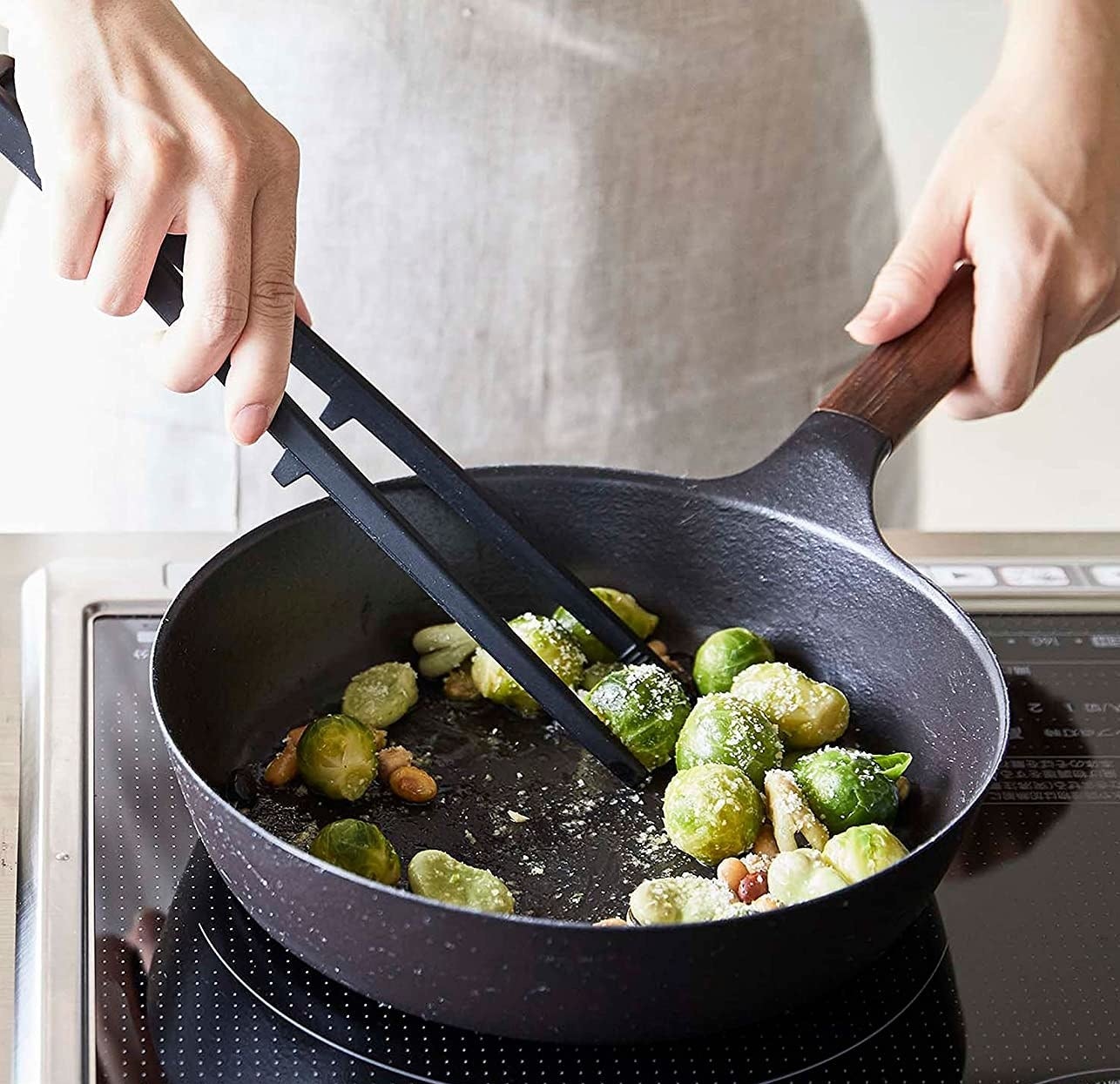 a person using the kitchen tongs to stir brussels sprouts