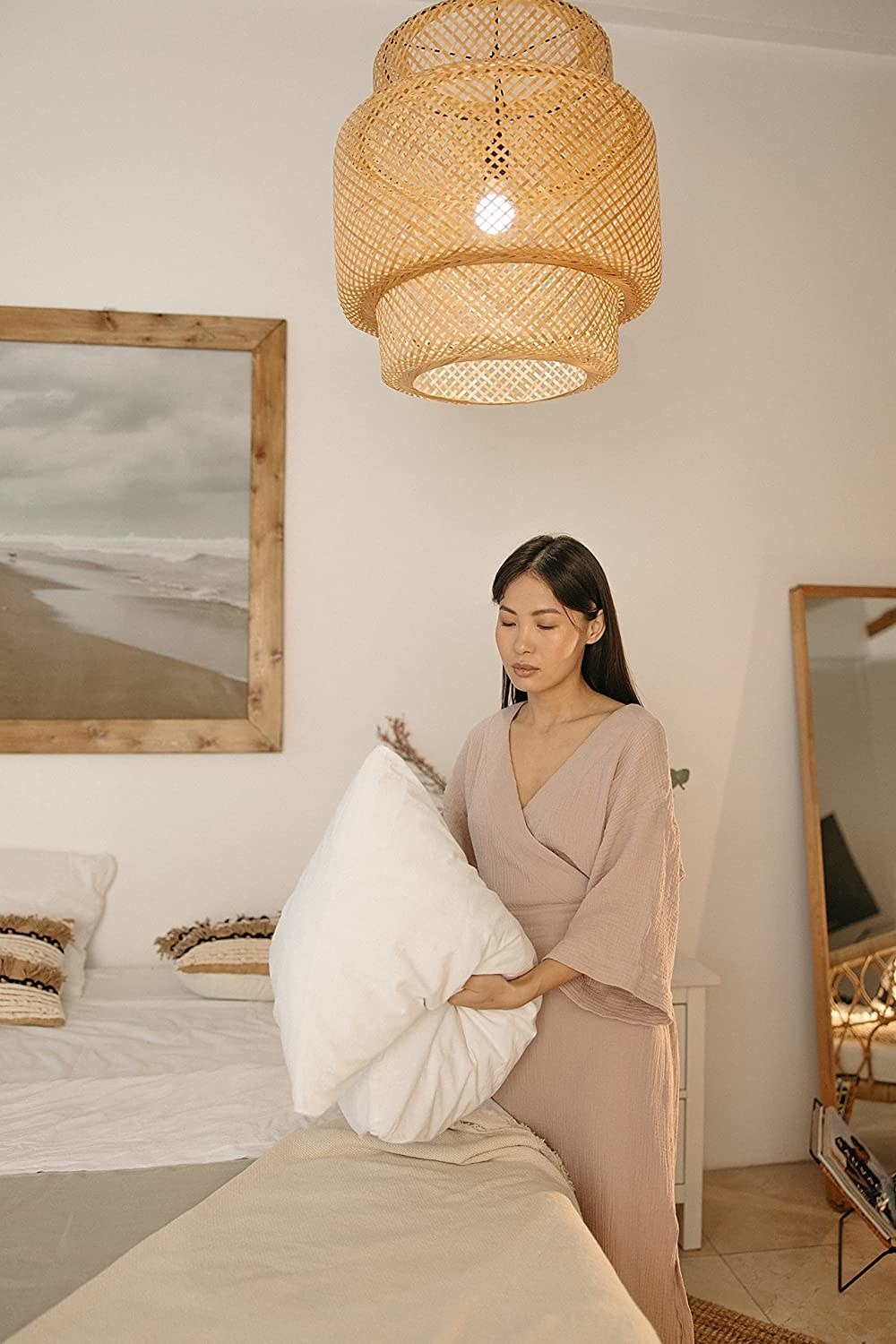 three tiered woven pendant light cover made with rattan. the image shows a model making their bed underneath the light.