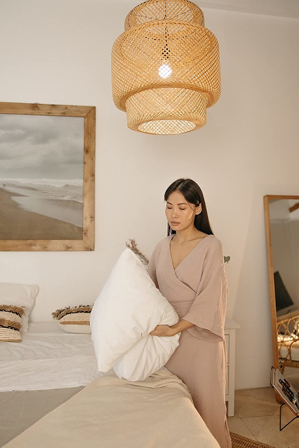 three tiered woven pendant light cover made with rattan. the image shows a person making their bed underneath the light.