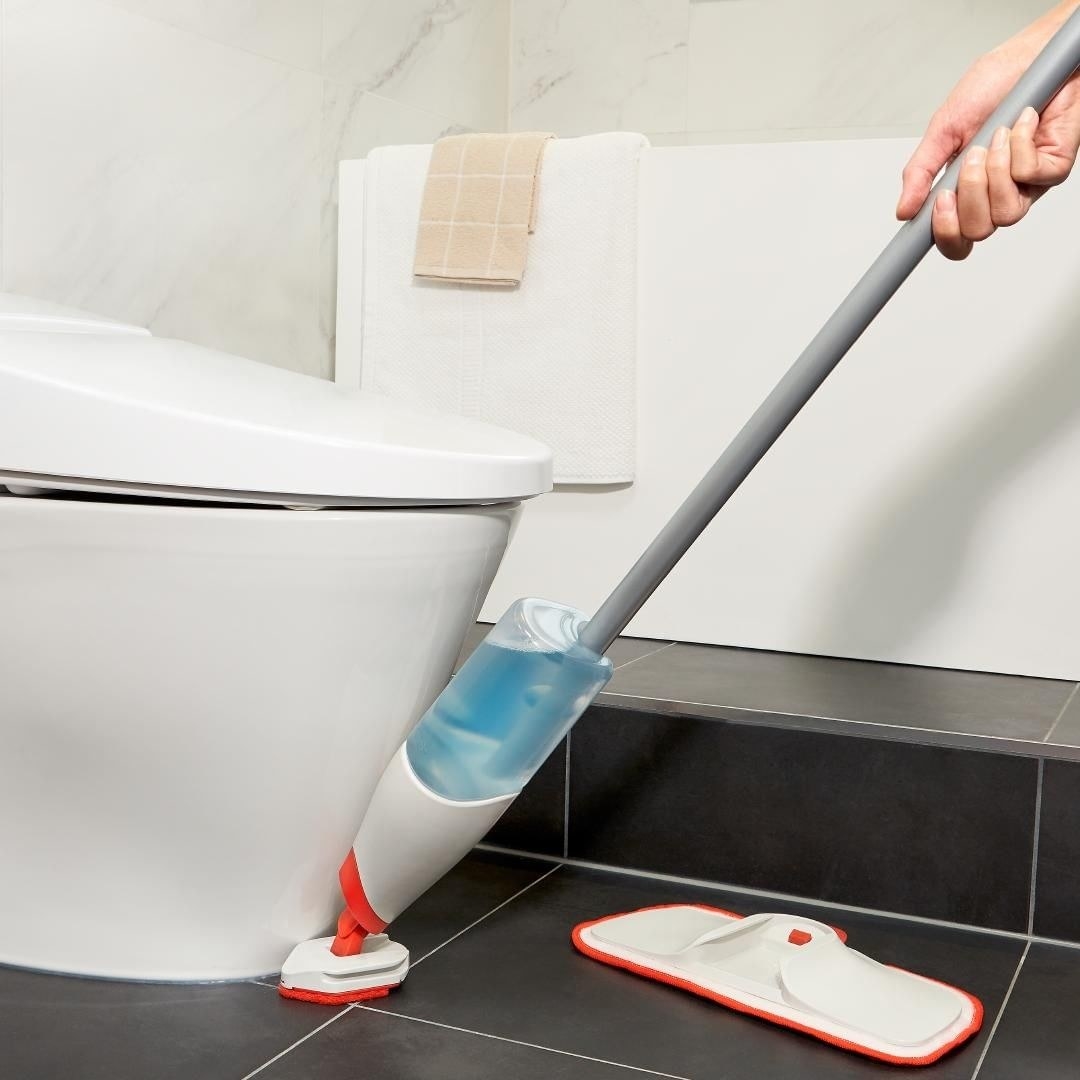 a person using the spray scrubber to clean around the toilet