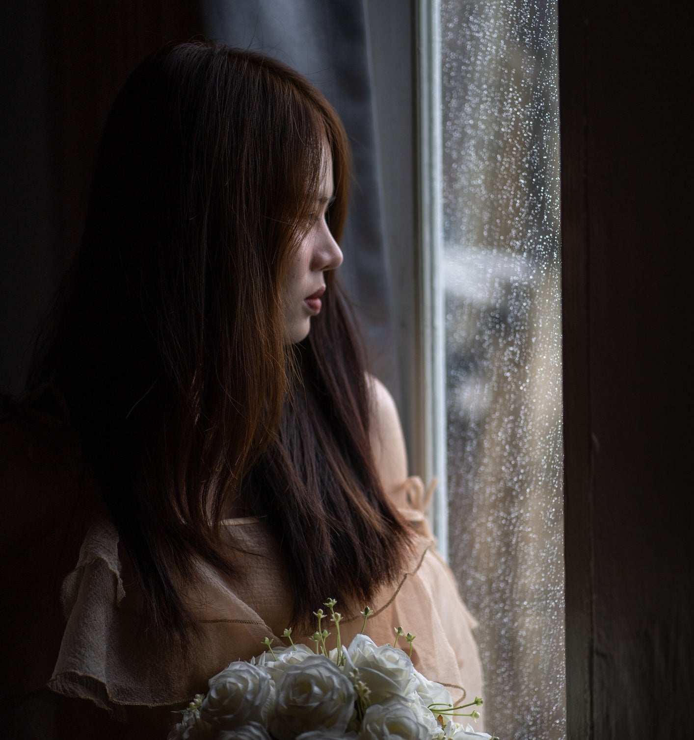 A woman holding roses stares out a window as it&#x27;s raining