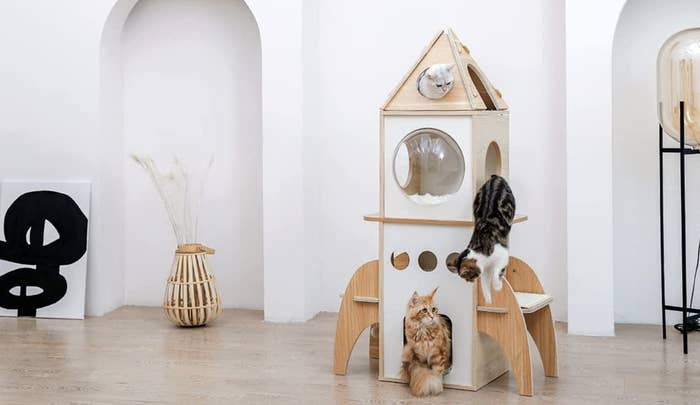 four level rocket ship shaped cat tree with three cats climbing on it