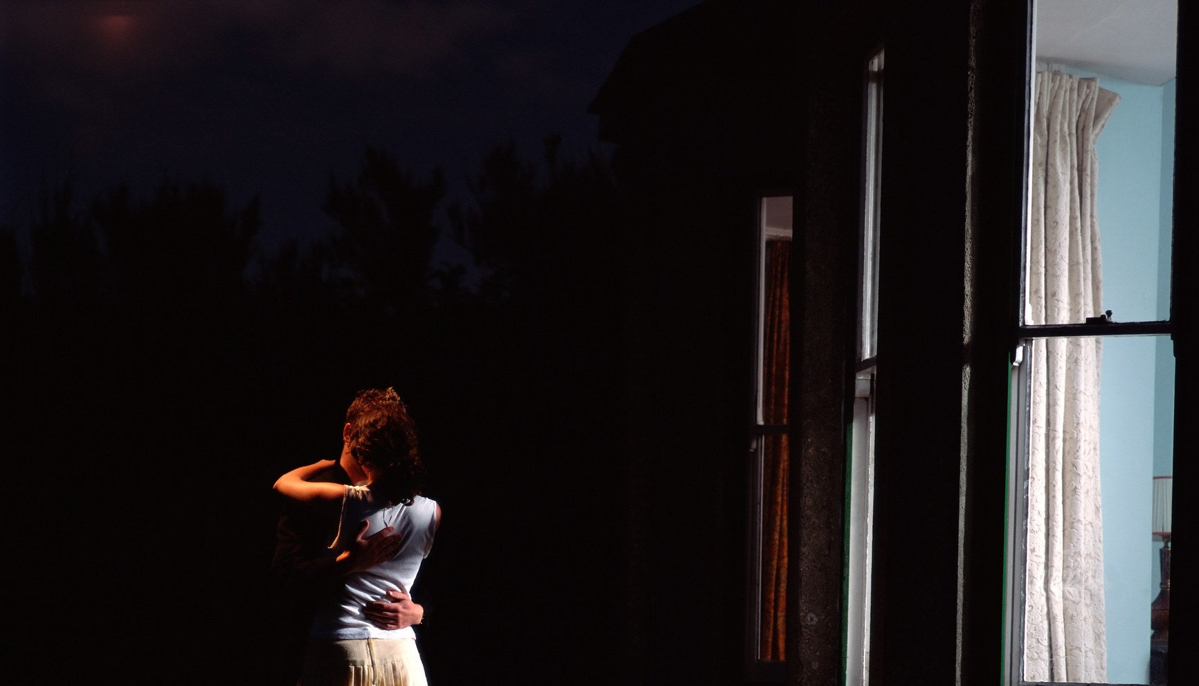 Couple hugging outside of home in dark