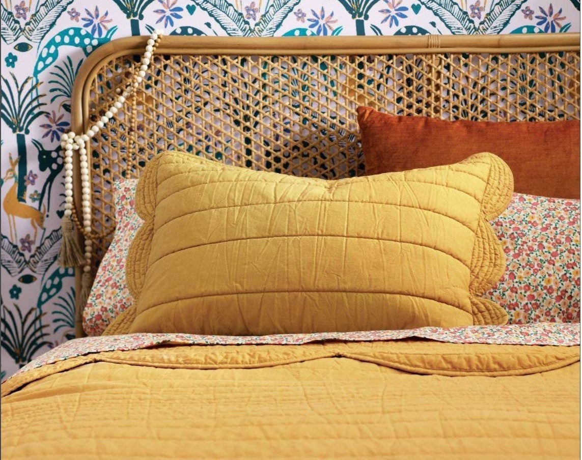 A colorful bed with a mustard scalloped pillow case