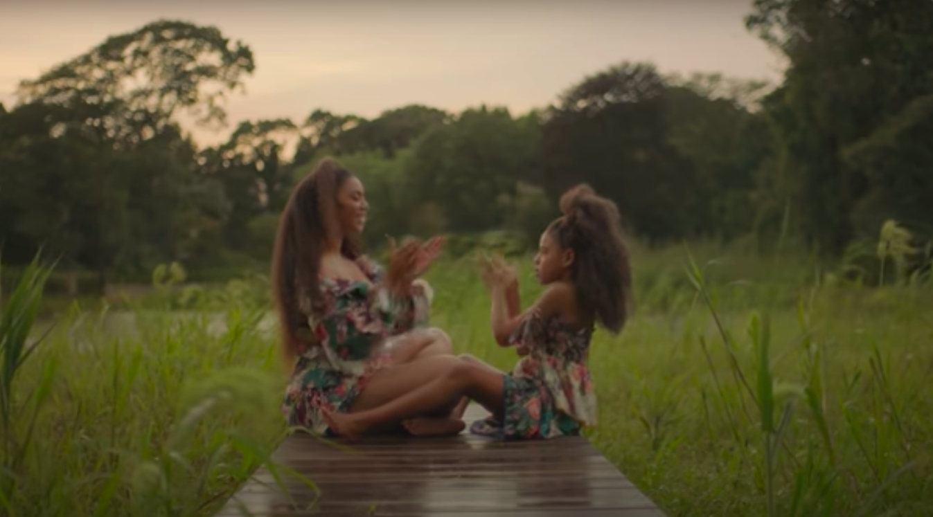Beyoncé and Blue playing a clapping game as they sit outside in a scene from the music video