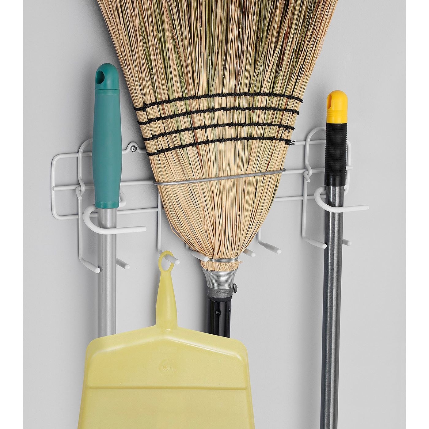several brooms and dustpans hung on the white wire rack