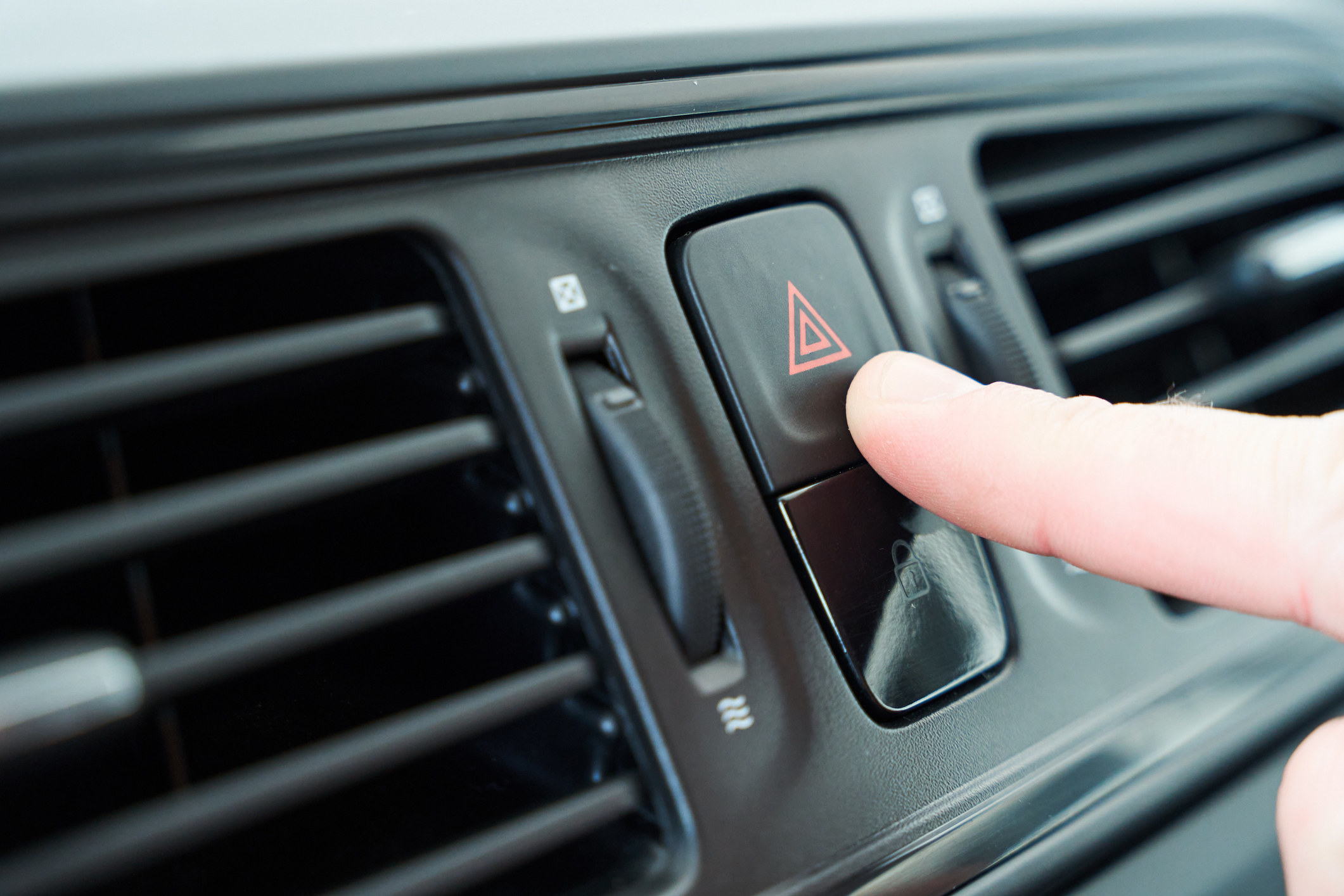 Close up view of the finger of a person pressing the red emergency button while driving a car