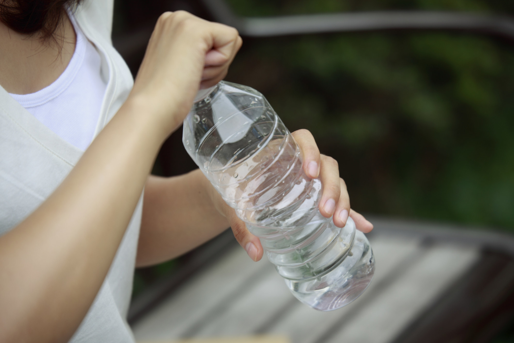 A young person opens a plastic water bottle to drink outside