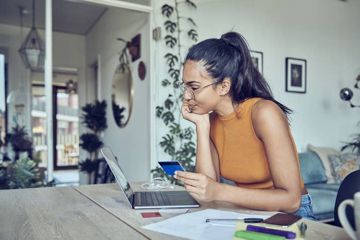 A woman holding a credit card and looking at her laptop as she sits in her home