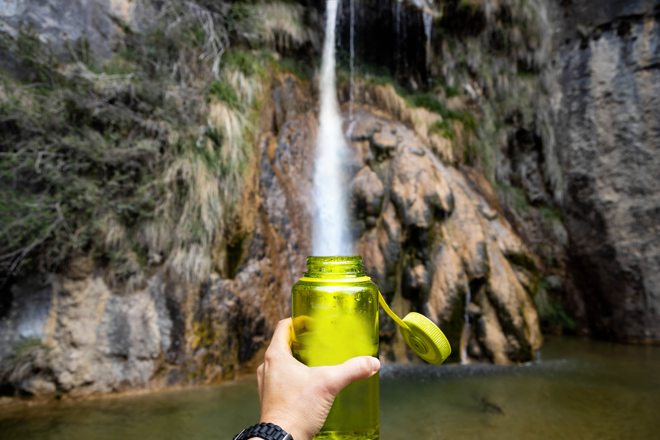 Person holding up a water bottle in front of a waterfall