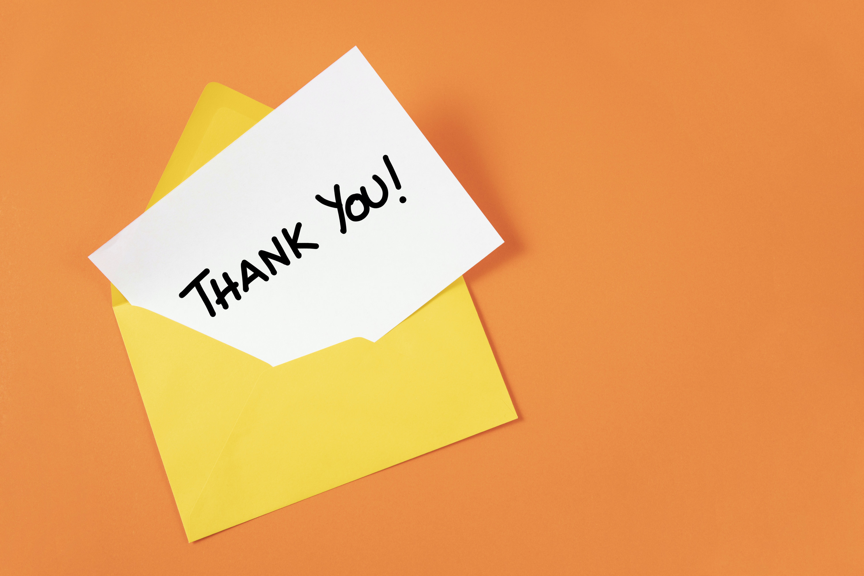 A white note coming out of a yellow envelope that says &quot;thank you&quot; against an orange background