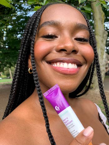 a model wearing the berry balm on their cheeks and lips, and holding up the tube