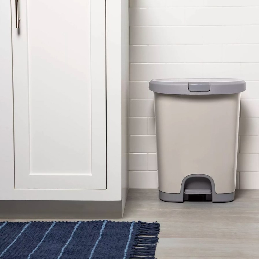 Gray trash can next to white cabinet and blue rug