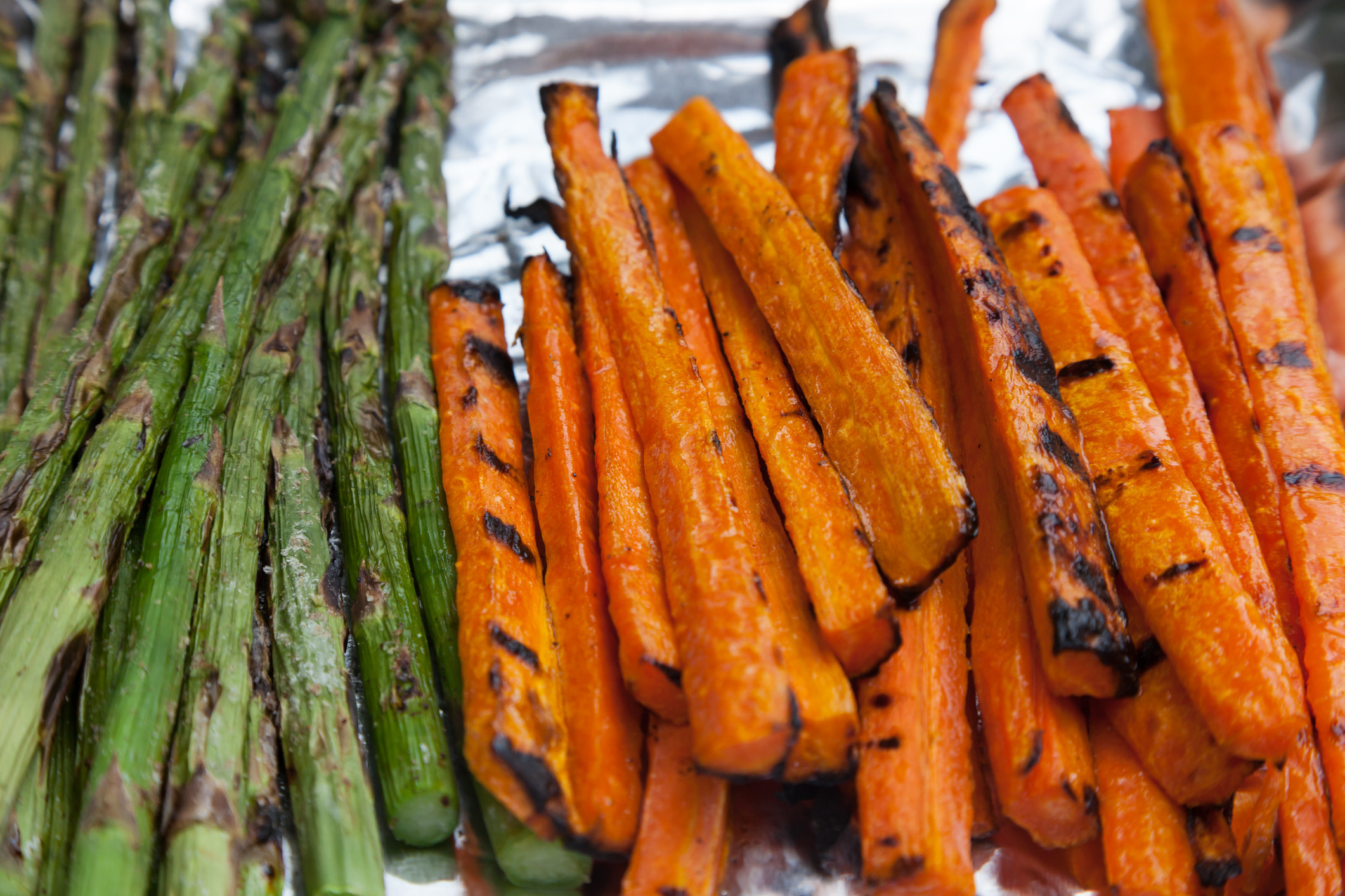Freshly grilled carrots and asparagus sit on foil.