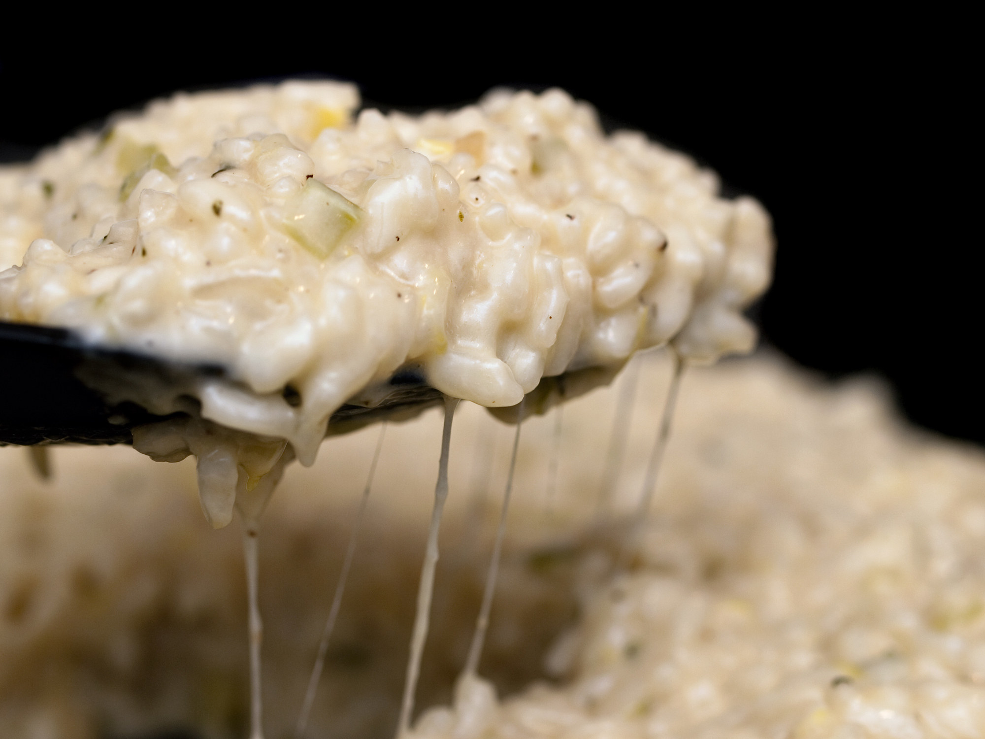 Close up of a spoonful of risotto with strings of cheese hanging from the spoon..
