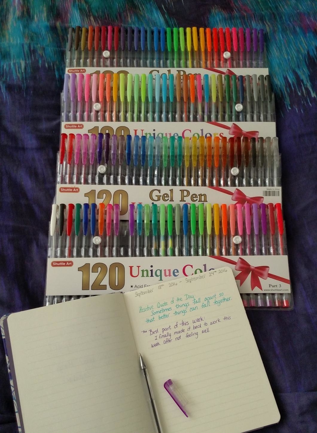 reviewer image of the gel pens next to an open notebook with notes written in blue and purple gel ink