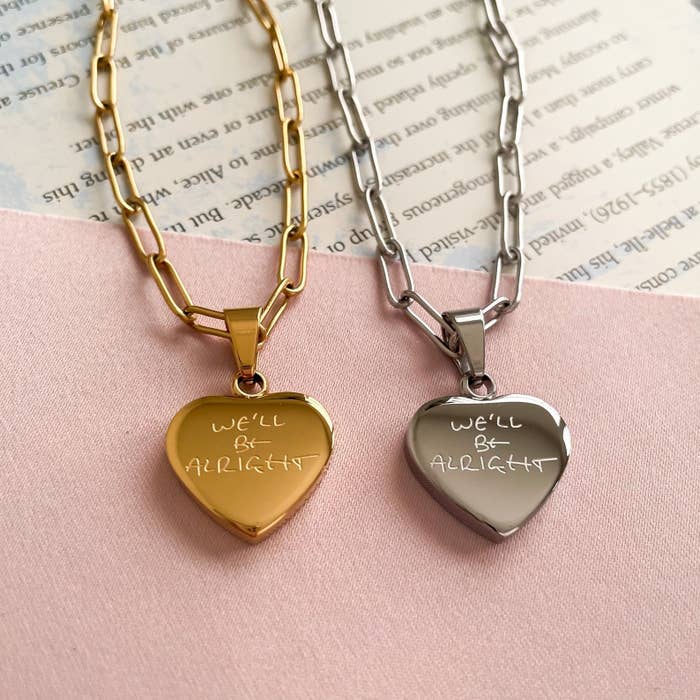 a gold and a silver we&#x27;ll be alright necklace against a soft pink background