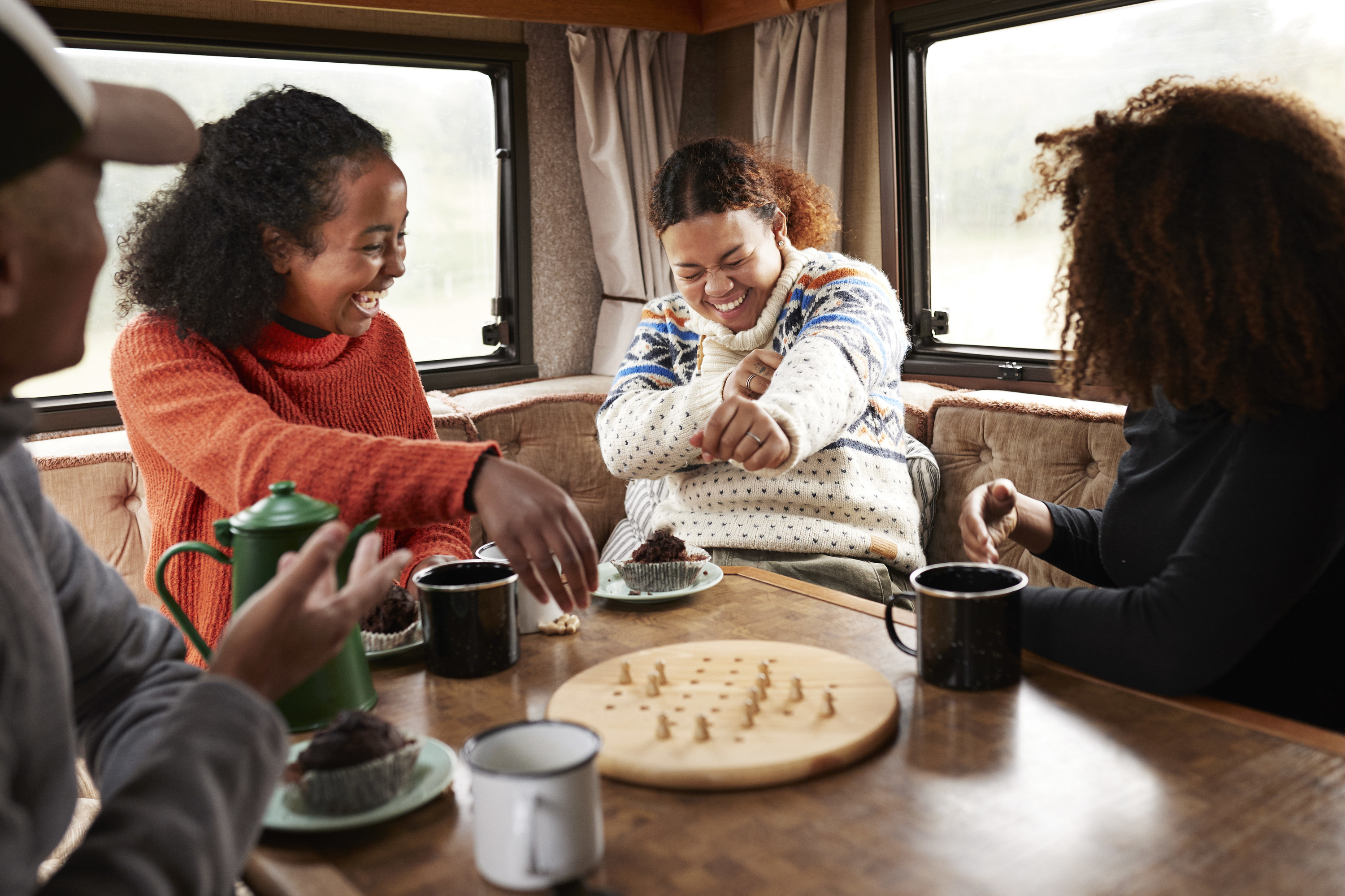 Cheerful friends having fun while playing board game at dining table in motor home during vacation