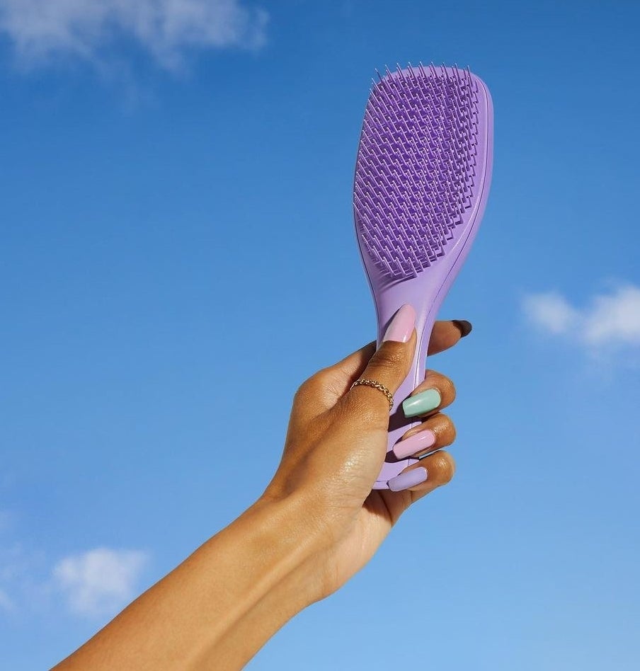 a person holding up the detangling brush against a bright sky